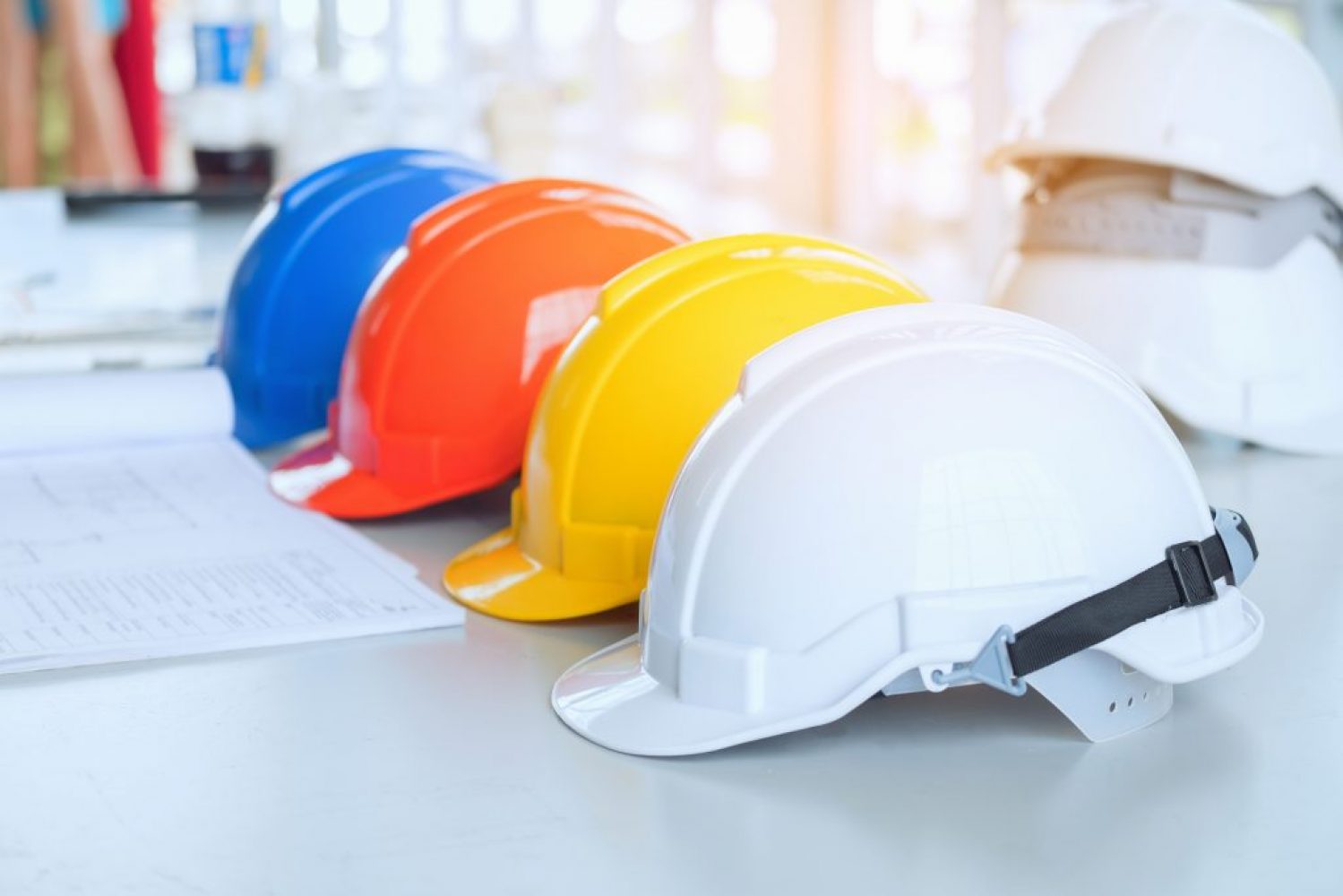 Red Yellow White and blue Safety hard hat on the blueprint with contract folder as background. Engineer work desk concept. The group of safety helmet and the blueprint at construction site